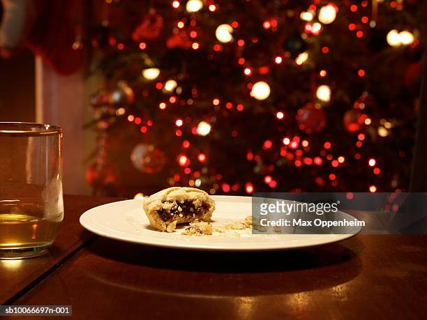 half eaten mince pie on empty plate, christmas tree behind - leftovers stockfoto's en -beelden