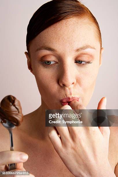 young woman with spoonful of creamy chocolate, licking finger - spoon stock pictures, royalty-free photos & images