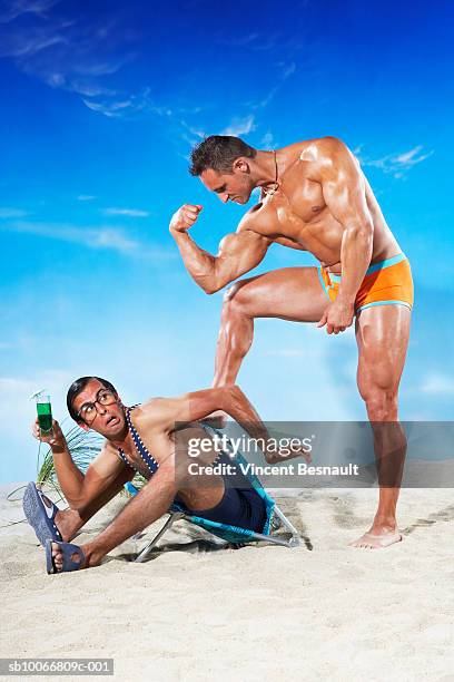 bodybuilder stepping on man's back on beach, side view - muscle men at beach stockfoto's en -beelden