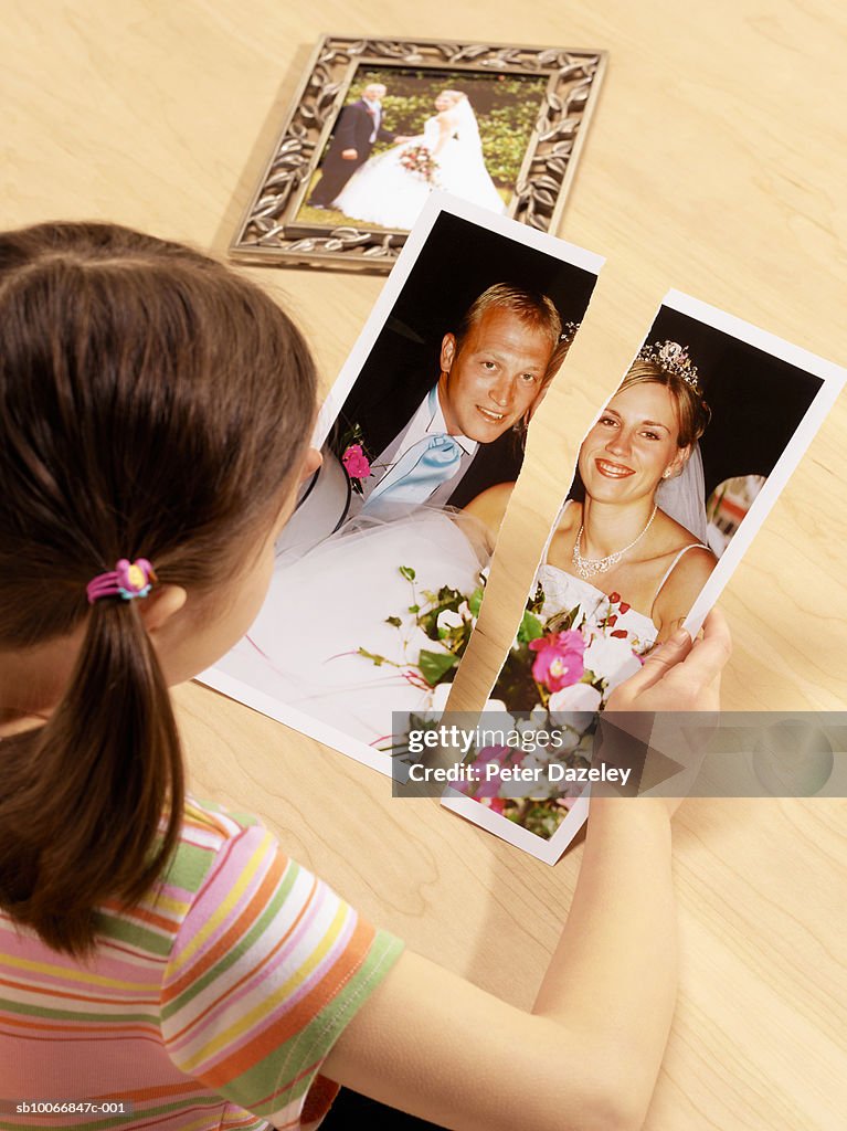 Girl (6-7) observing torn photograph of separated parents wedding