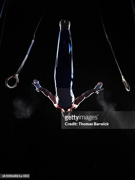 teenage (16-17) male gymnast dismounting rings on black background - male gymnast photos et images de collection