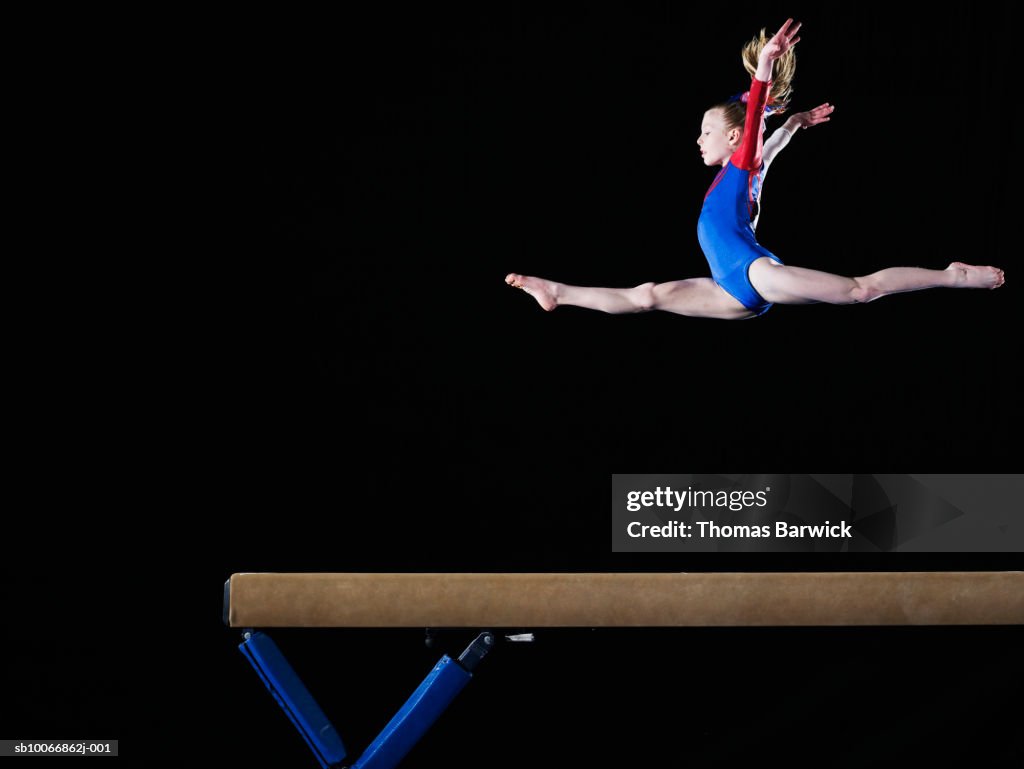 Gymnast (9-10) leaping on balance beam