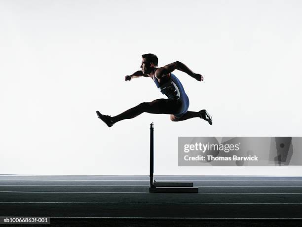 male runner jumping over hurdle - venciendo la adversidad fotografías e imágenes de stock