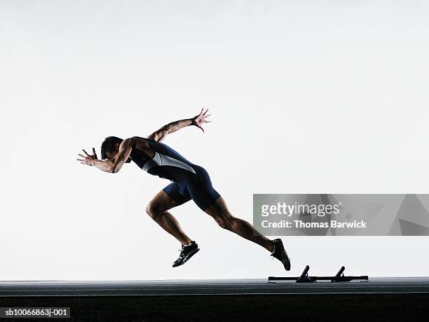 male runner leaving starting block, side view - línea de salida fotografías e imágenes de stock