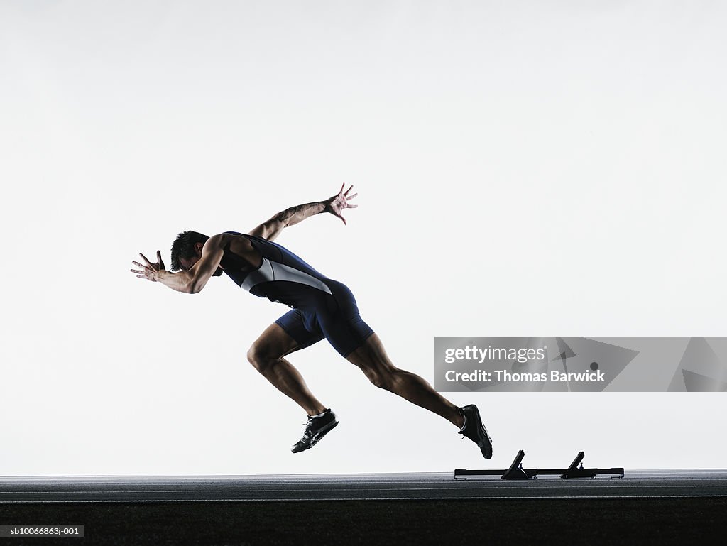 Male runner leaving starting block, side view