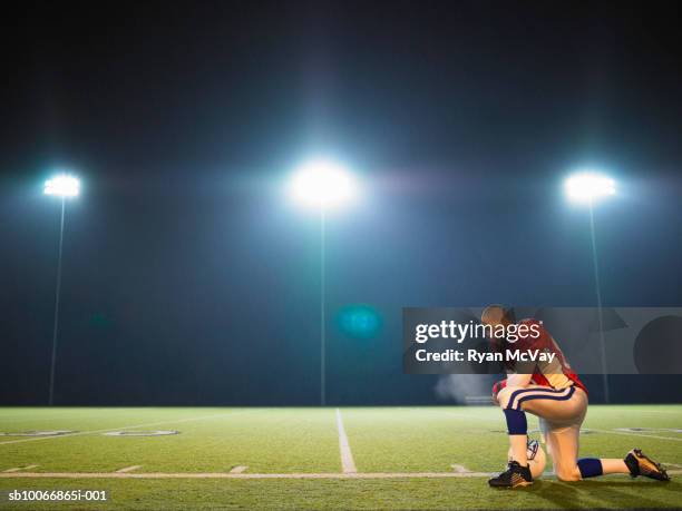 american football player kneeling on pitch, side view - knielen stockfoto's en -beelden