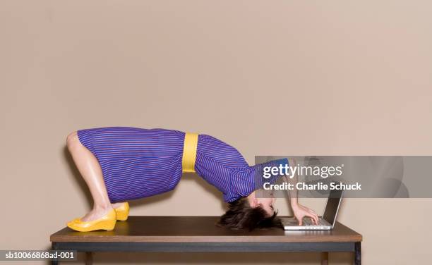 woman bending over backwards on table while working on laptop - contorsioniste photos et images de collection