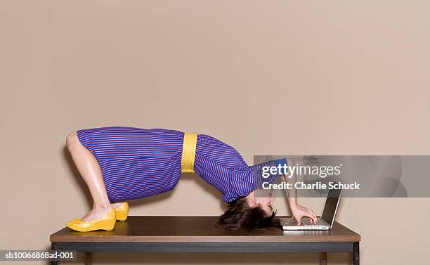 woman bending over backwards on table while working on laptop - flessibilità foto e immagini stock