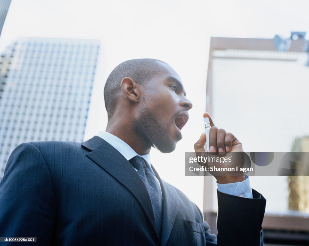 Businessman using breath freshener outdoors, low angle view