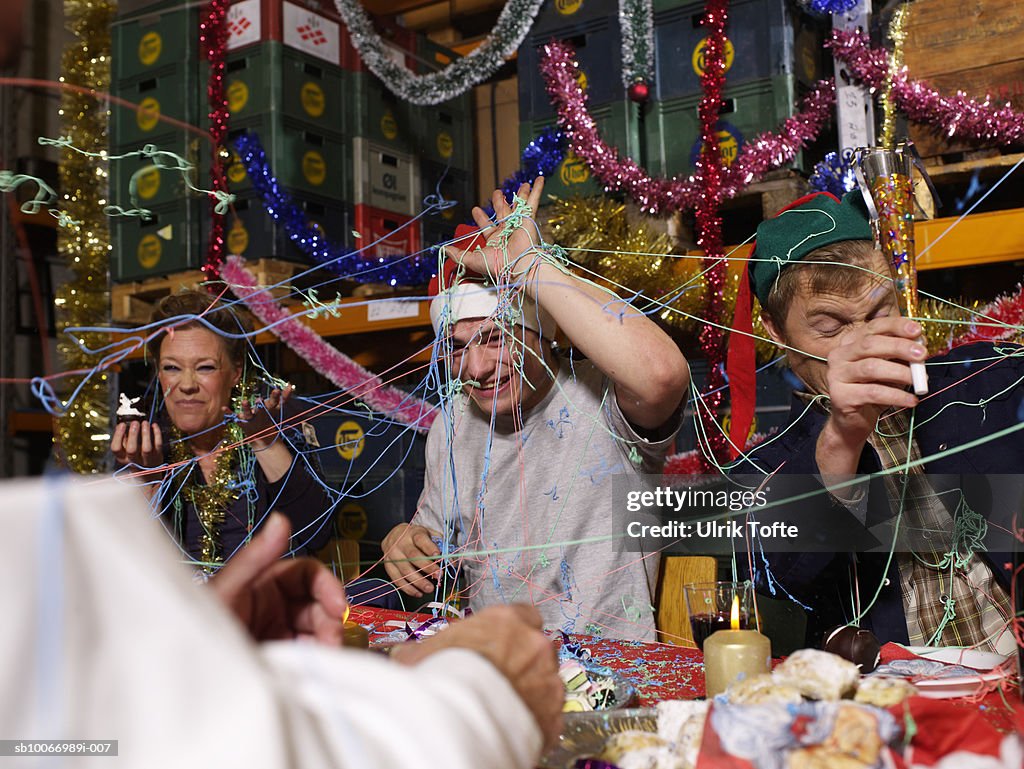 Three people covered in party streamers laughing at charismas table in warehouse