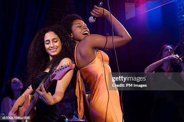 woman singing with microphone and guitar player on stage with band in background - fun band stock pictures, royalty-free photos & images