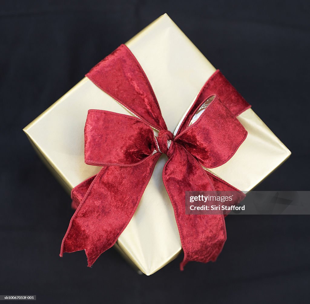 Gift with red bow on black background, overhead view, close-up