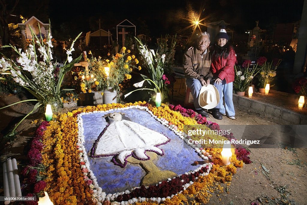 Mexico, Oaxaca, Grandfather with granddaughter (6-7) at cemetery for Day of the Dead, smiling, portrait