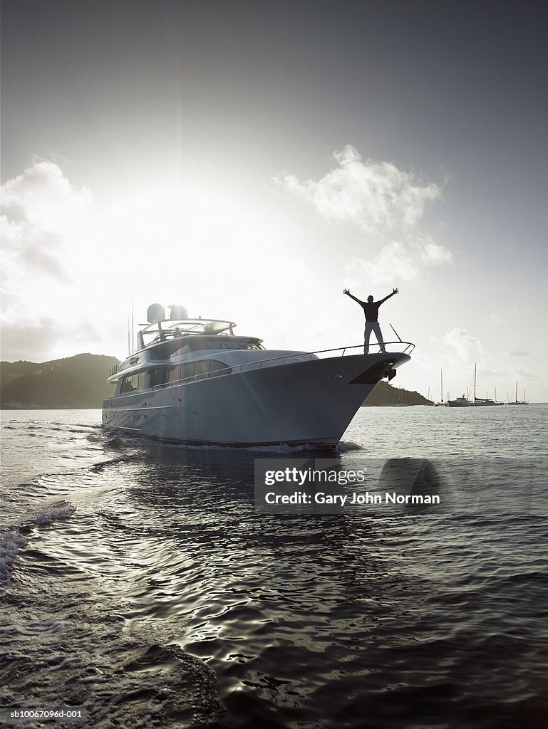 Man standing on bow of yacht with arms outstretched