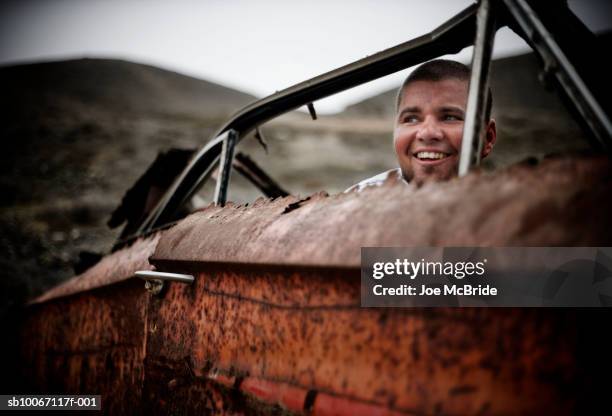 man sitting in junk car, smiling - rusty car stock-fotos und bilder