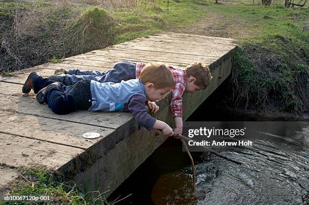 boys (2-5) lying on bridge playing in water with stick - voetgangersbrug stockfoto's en -beelden