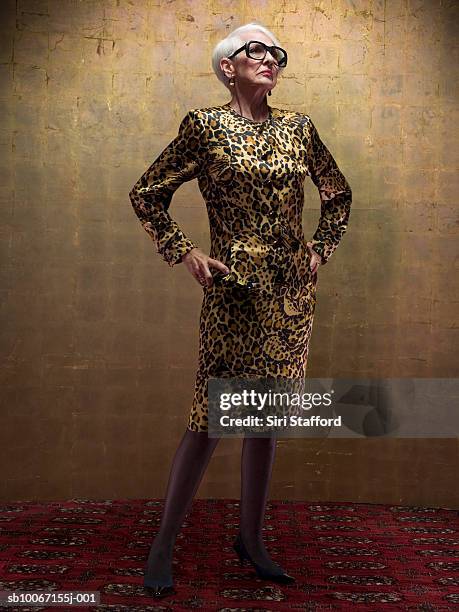 senior woman wearing leopard print dress standing in studio - hand an der hüfte stock-fotos und bilder