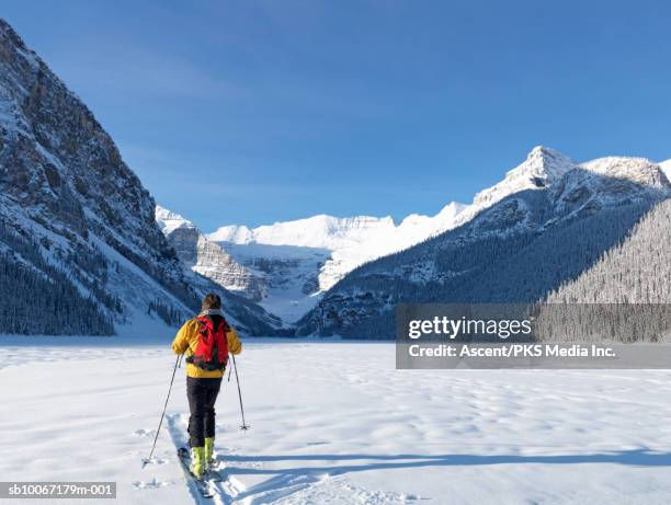 canada, alberta, banff national park, man skiing across lake louise towards mt temple and lefroy - banff skiing stock pictures, royalty-free photos & images