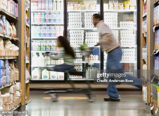 man pushing daughter (10-11) in shopping trolley in supermarket, side view (blurred motion) - supermarket trolley female stock-fotos und bilder