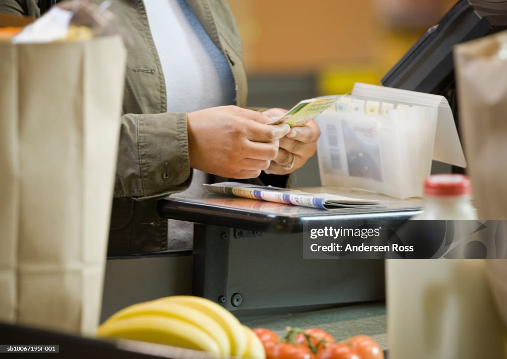 Woman sorting coupons at supermarket, close-up, mid section