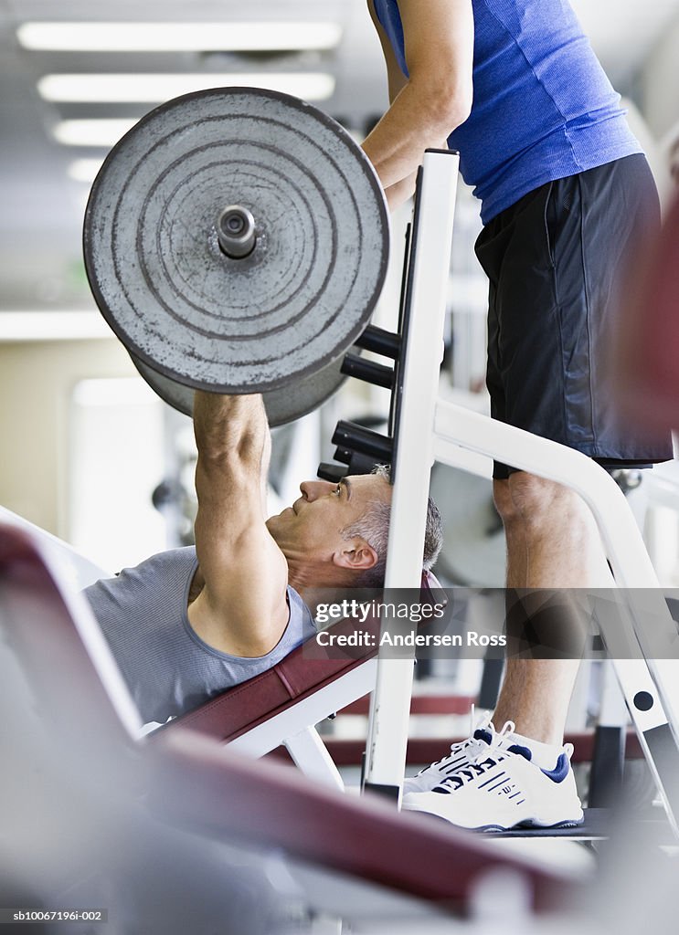 Man lifting weights, friend assisting, side view