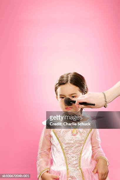 woman powdering nose of girl (6-7) on pink background - schoonheidswedstijd stockfoto's en -beelden