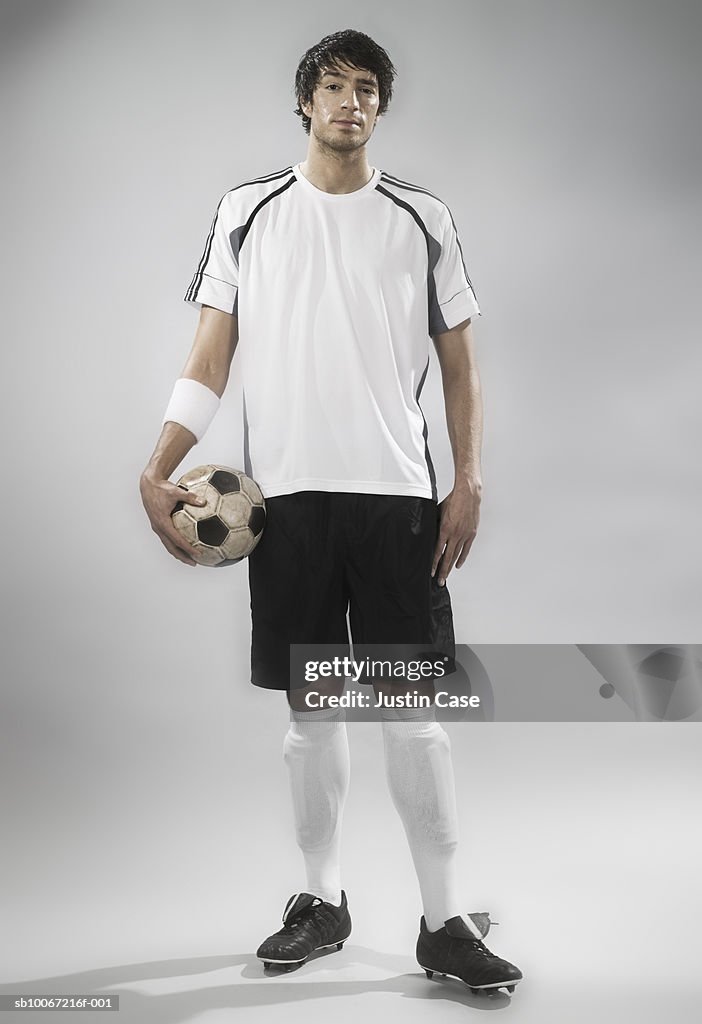 Soccer player holding soccer ball, studio shot, portrait