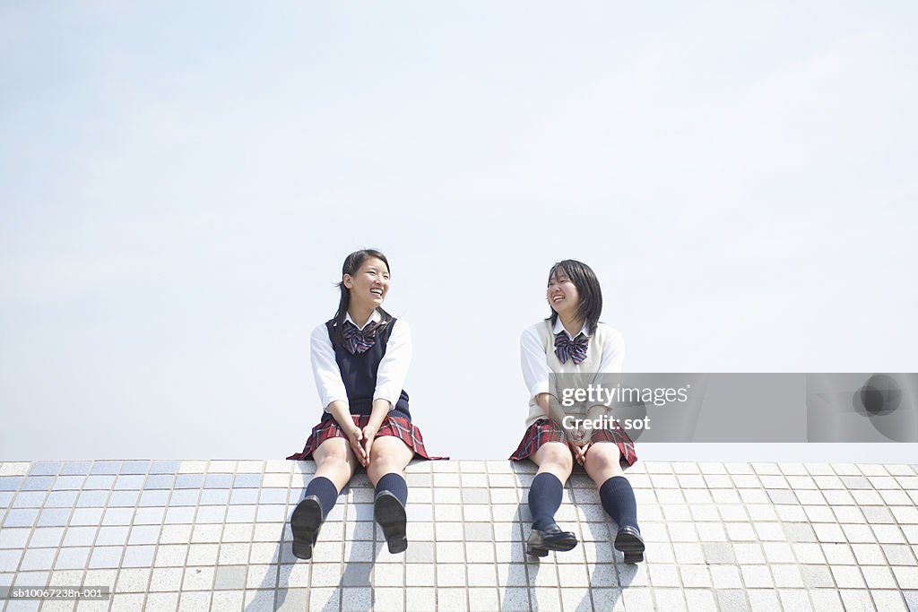 Two female high school students (17-18) sitting on top of tiled wall