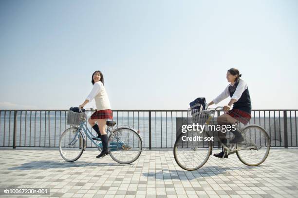 two female high school students (17-18) riding bikes by seafront - female high school student stock pictures, royalty-free photos & images