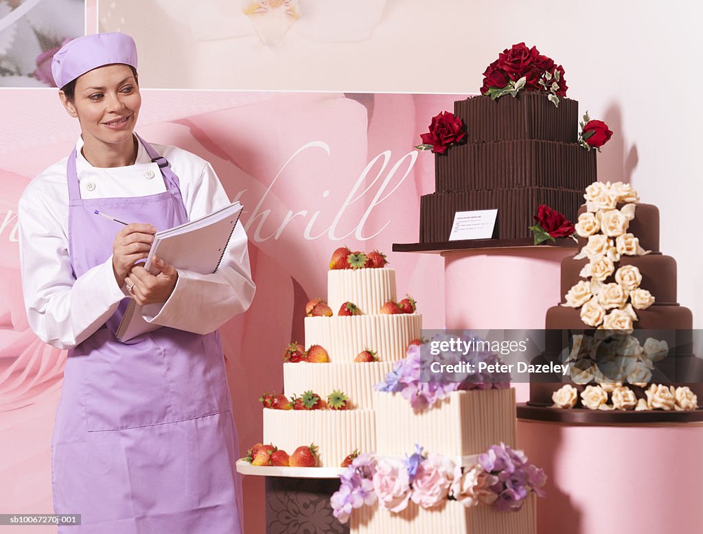 Cake maker in cake shop, holding notebook, smiling