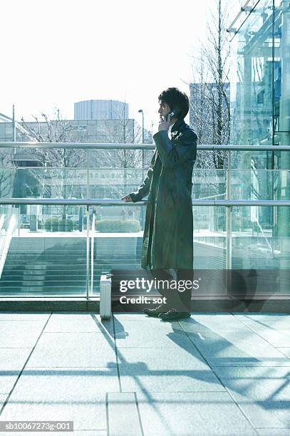 businessman using mobile phone in office, side view - オーバーコート ストックフォトと画像
