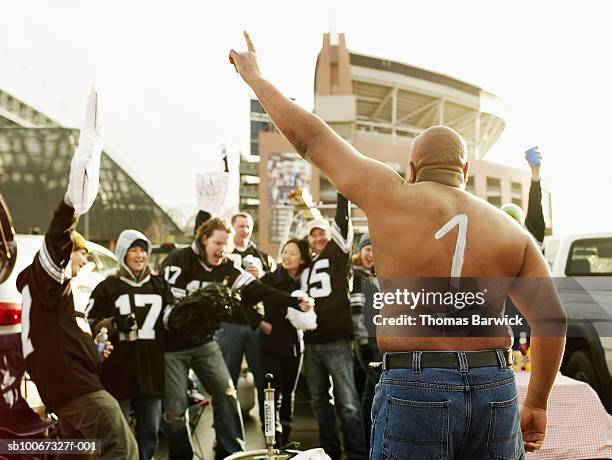 man with '1' painted on back cheering with friends at tailgate party - tailgating stock pictures, royalty-free photos & images