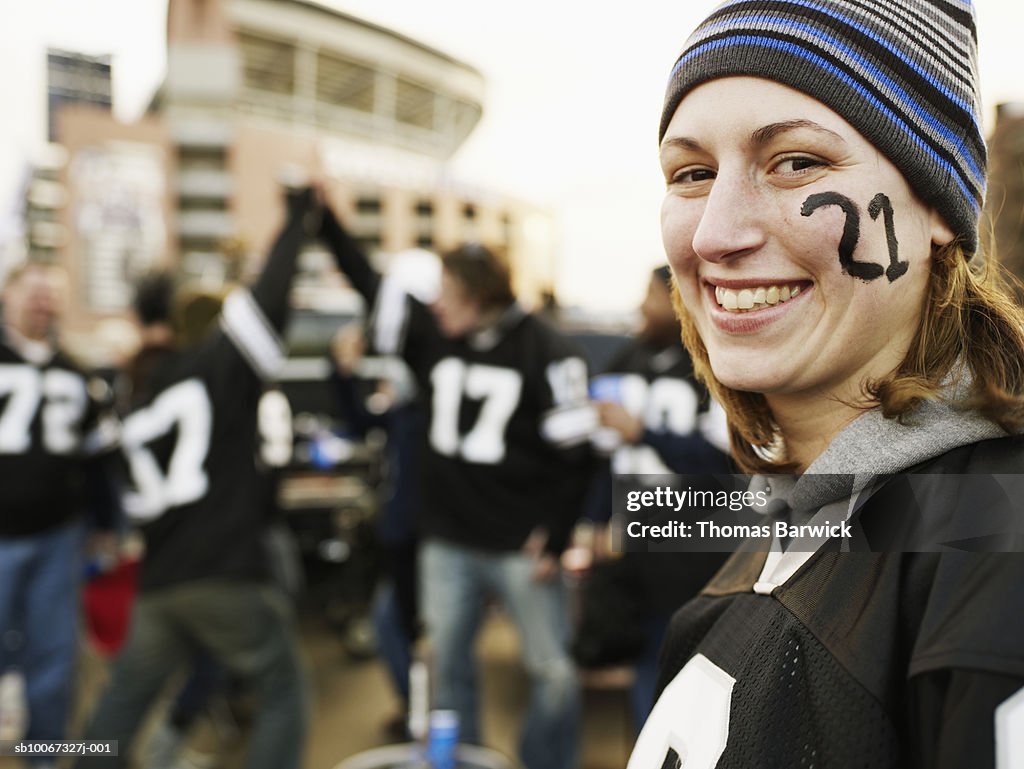 Woman with face paint smiling at tailgate party, friends in background