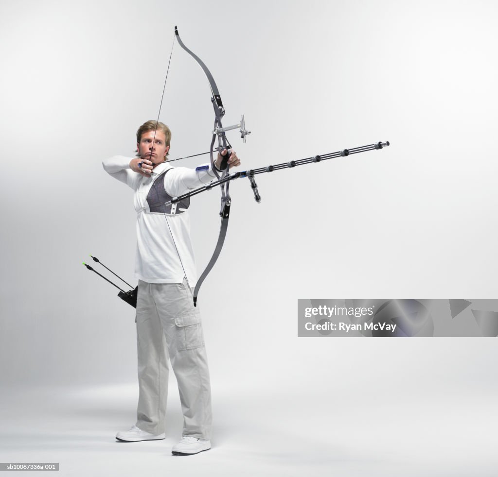 Young archer pointing bow, studio shot