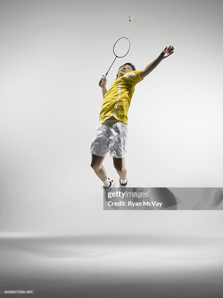 Man jumping to hit badminton birdie, studio shot