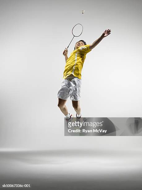 man jumping to hit badminton birdie, studio shot - sportsman imagens e fotografias de stock