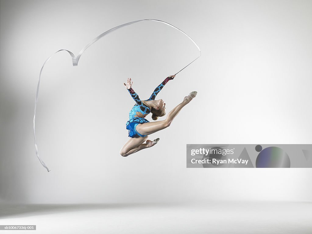 Female gymnast (14-15) leaping with dance ribbon, studio shot