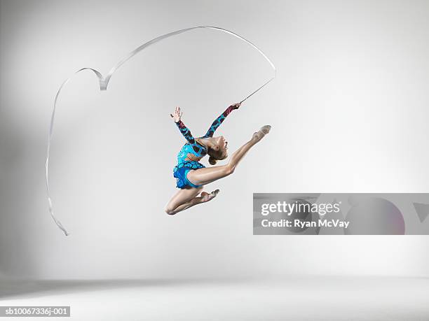 female gymnast (14-15) leaping with dance ribbon, studio shot - acrobat stock pictures, royalty-free photos & images