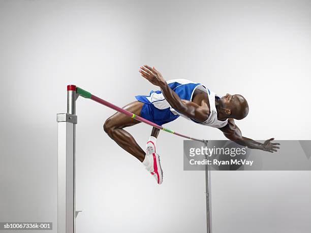 man jumping over high jump, studio shot - leichtathletik stock-fotos und bilder