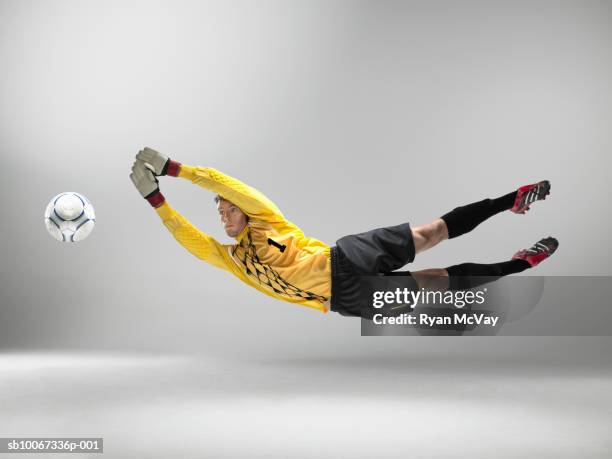 goal keeper jumping to catch football (studio shot) - torwart stock-fotos und bilder