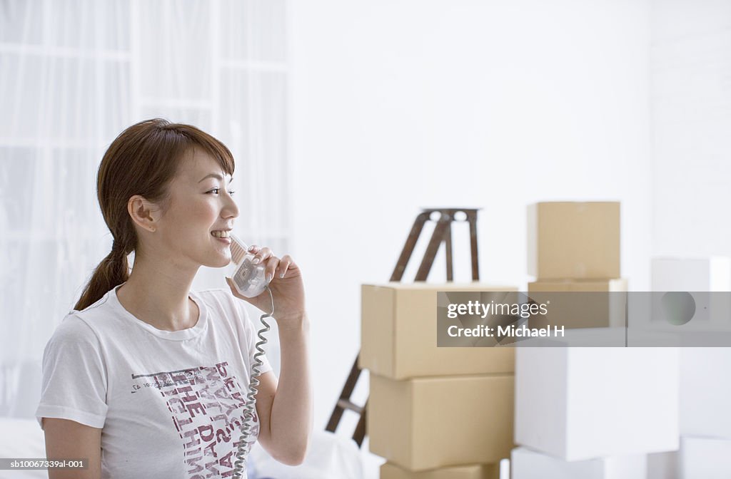 Young woman using telephone in room with cardboard boxes