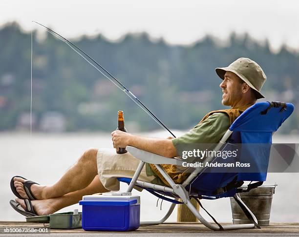 man fishing at dock, holding beer bottle, side view - fishing ストックフォトと画像
