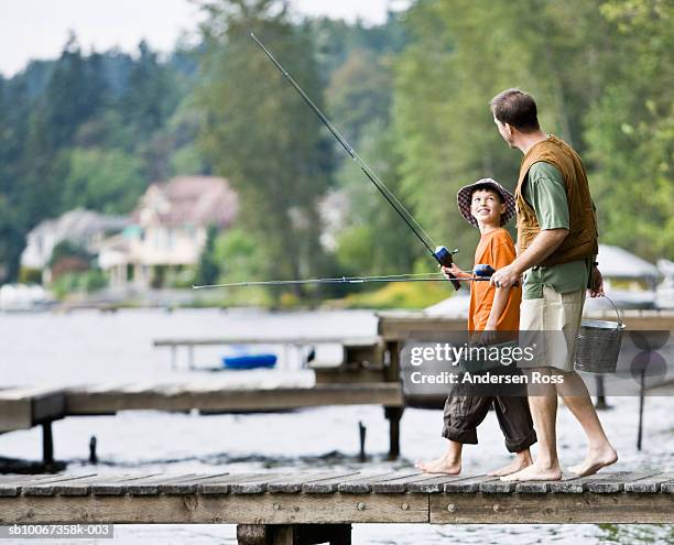 father and son (10-11) carrying fishing rods on pier - ventil stockfoto's en -beelden