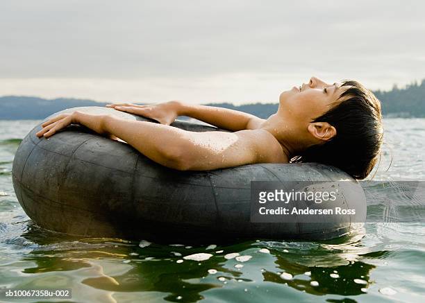 teenage boy (14-15) floating in rubber ring, side view - very young tube stock pictures, royalty-free photos & images