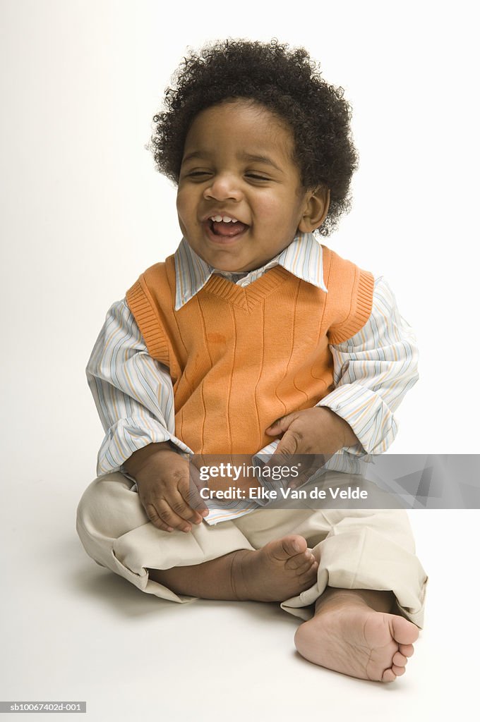 Baby boy (12-17 months) sitting on white background and laughing