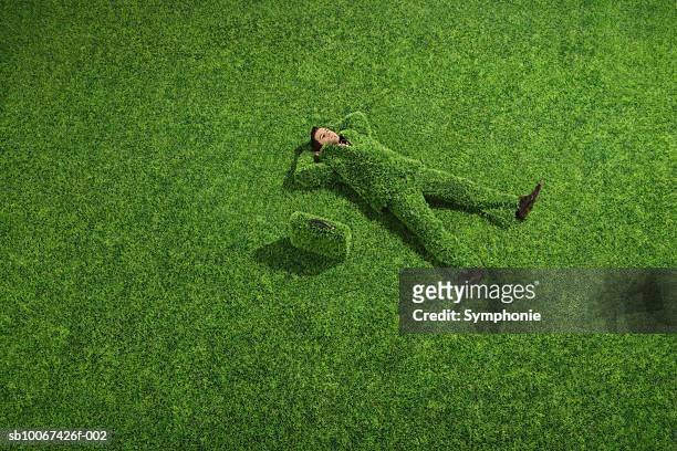 young busienss man wearing suit made of grass laying on lawn, elevated view - traje verde fotografías e imágenes de stock