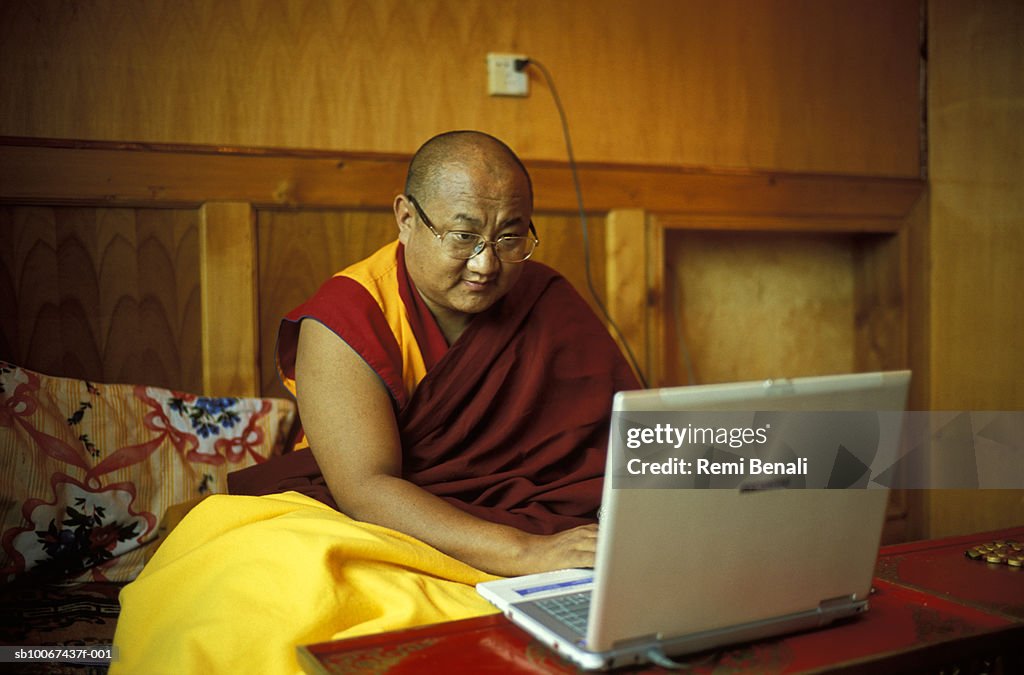 China, Sichuan Province, Litang, Rimpoche Xiaba monk using laptop in bedroom