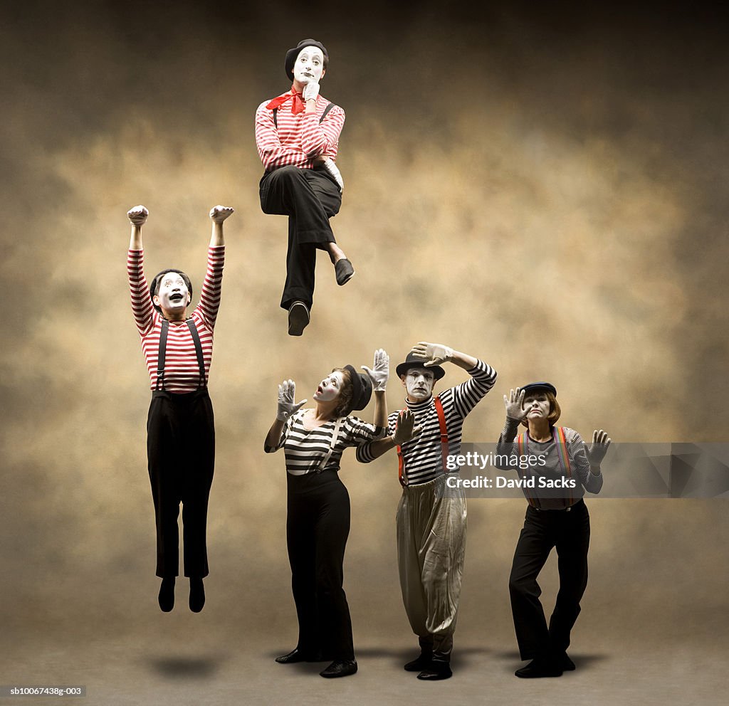Group of mimes stuck behind wall, one hanging, another sitting on top