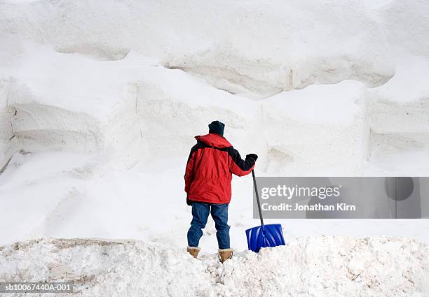 man with snow shovel facing large pile of snow, rear view - spade stock pictures, royalty-free photos & images