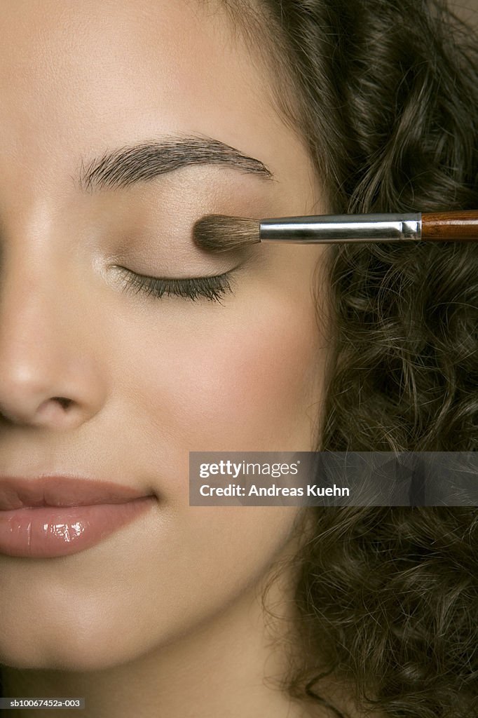 Young woman applying eyeshadow, eyes closed, close-up
